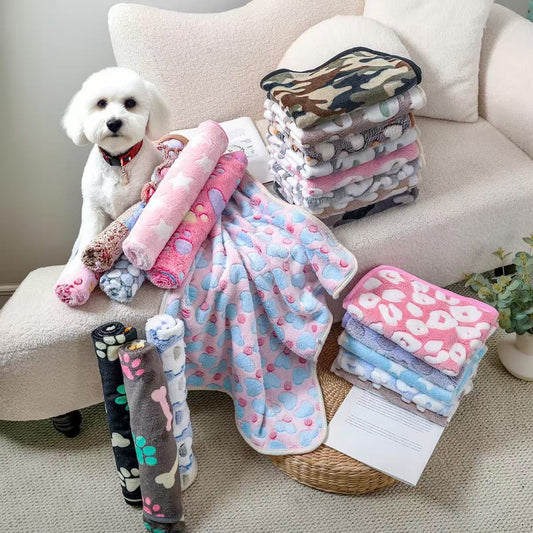Blankora Snuggle Square mini fleece pet mats in assorted patterns stacked on a sofa with a small white dog